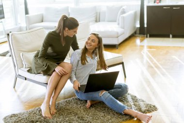 Genç kadın kanepe online alışveriş Web sitesi tarama yaparken rahatlatıcı üzerinde oturan gülümseyen