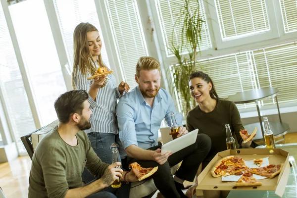 Group of young people eating pizza, drinking cider and watching digital tablet in the room