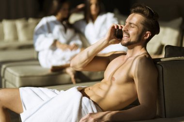Yakışıklı delikanlı içinde havlu iki kadın ile odasında cep telefonu kullanarak
