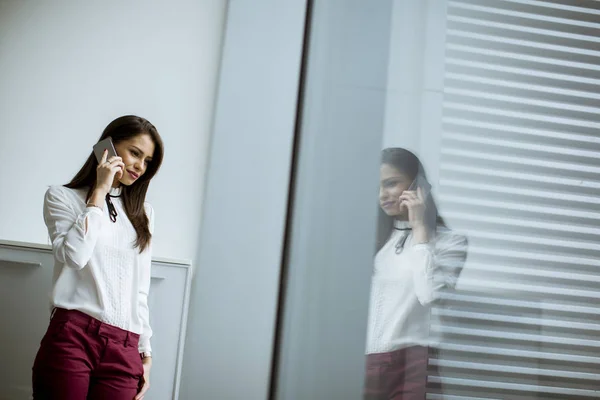 年轻的女商人站在办公室里用手机 — 图库照片
