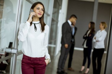 Genç işkadını üstünde hareket eden telefon arka planda konuşurken diğer iş adamları ise ofiste konuşmak