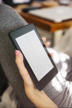 Genç kadın kanepede bir ebook okuyucu kullanarak