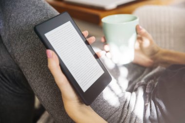 Kahve içme ve kanepe bir ebook okuyucu kullanarak genç kadın