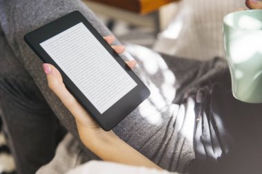Kahve içme ve kanepe bir ebook okuyucu kullanarak genç kadın