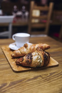 Fincan cappuccino kahve ve kruvasan ahşap bir tabloda, üstten görünüm