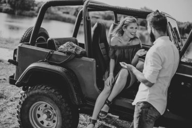 Genç kadın ve adam arabanın yakınında açık yaz gününde eğleniyor