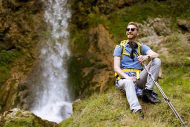 Yakışıklı genç Kızıl saçlı uzun yürüyüşe çıkan kimse dinlenmek için bir dağ şelale durdu
