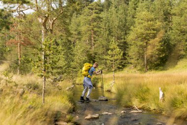 Güneşli bir günde bir yürüyüş sırasında bir dağ dere Dişileştirilmiş genç adam haçlar