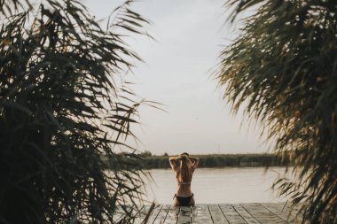 Gölde bir iskelede oturan bikini çekici genç kadın geri görünüm