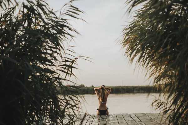 Gölde bir iskelede oturan bikini çekici genç kadın geri görünüm