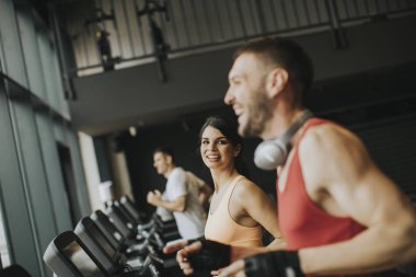 Modern bir spor salonu içinde koşu bandı üzerinde çalışan genç Çift