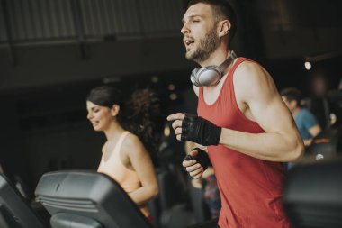 Modern bir spor salonu içinde koşu bandı üzerinde çalışan genç Çift