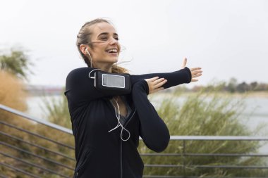 Açık havada müzik dinlerken kollarına uzanan kadın genç atlet