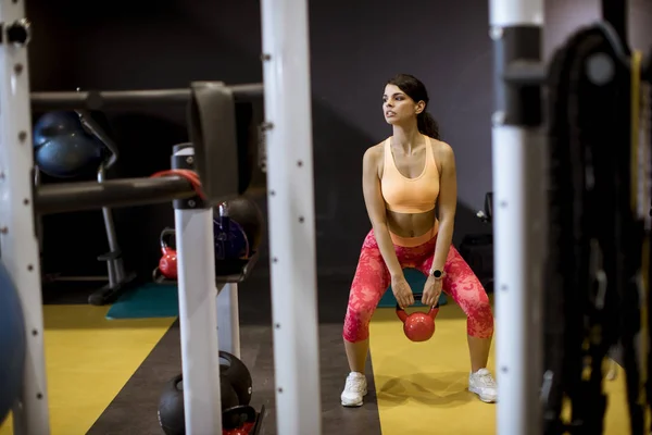 Young woman doing arm exercise with Kettler dumbbell all in front of her at gym