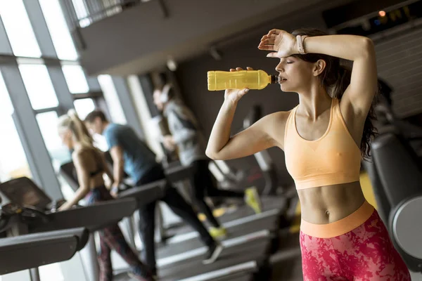 Healthy women in yellow sport shirt are drinking water at the gym