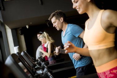 Modern bir spor salonu içinde koşu bandı üzerinde çalışan gençlerin grup