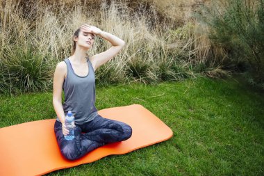 Genç kadın parkta oturan ve egzersiz sonrası içme suyu