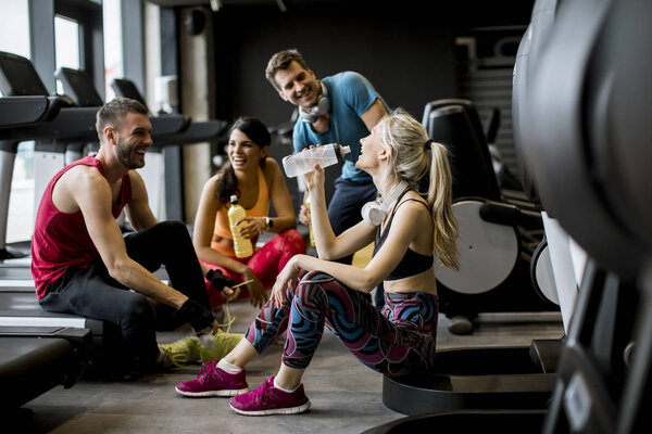 Group of young people in sportswear talking and laughing together while sitting on the floor of a gym after a workout