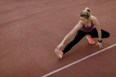 Dışarıdaki sahada ısınma egzersizleri yapan ve bacaklarını açan genç bir kadın.
