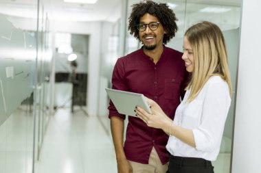 Genç Afrikalı Amerikalı iş adamı ve Kafkasyalı iş kadını. Tablet bilgisayarlı, ofisinde duruyor.