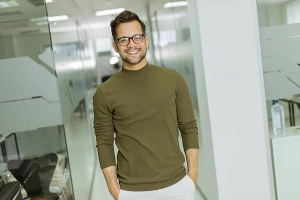 Bonito sorridente jovem empresário em óculos de pé no escritório — Fotografia de Stock