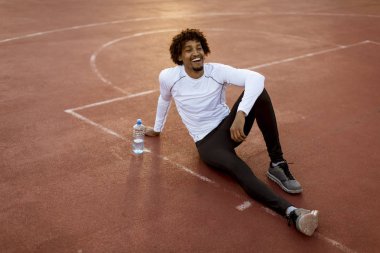 Basketbol sahasında oturan kıvırcık saçlı çekici siyah adam yakın