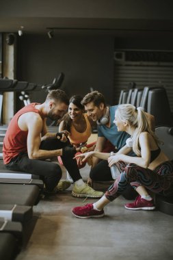 Spor giyimli bir grup genç, antrenman dan sonra spor salonunun zemininde otururken birlikte konuşup gülüyor