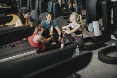 Spor giyimli bir grup genç, antrenman dan sonra spor salonunun zemininde otururken birlikte konuşup gülüyor