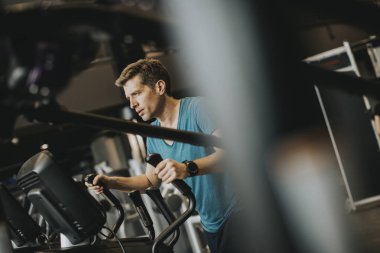 Genç adam spor fitness kulübünde eliptik çapraz antrenör üzerinde egzersiz yapıyor.