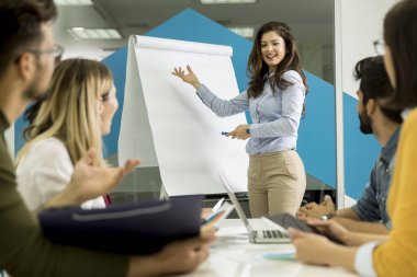 Kendinden emin genç takım lideri, küçük başlangıç ofisinde flip chart'a göre gruplandırılan bir grup genç iş arkadaşına sunum yapıyor