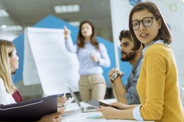 Kendinden emin genç takım lideri, küçük başlangıç ofisinde flip chart'a göre gruplandırılan bir grup genç iş arkadaşına sunum yapıyor