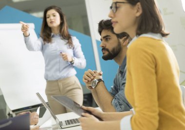 Kendinden emin genç takım lideri, küçük başlangıç ofisinde flip chart'a göre gruplandırılan bir grup genç iş arkadaşına sunum yapıyor