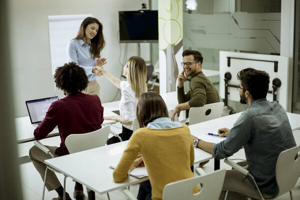 Smiling young woman standing near whiteboard and shaking hand to her female colleague in the small startup office