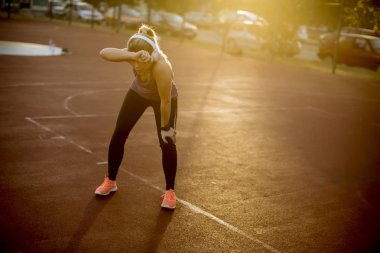 Gün batımında oyun alanında dururken aktif bir fitness eğitimi nden sonra dinlenen güzel genç kadın