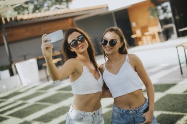 Sıcak yaz gününde cep telefonuyla selfie çeken genç kadınlar.