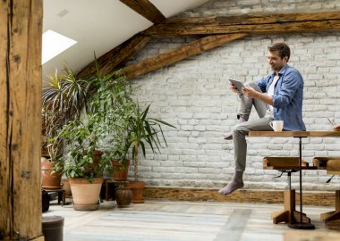 Rustik odada masada otururken dijital tablet kullanarak yakışıklı genç adam