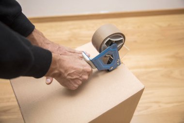 Bir nakliye kutusunu mühürlemek için bant dağıtıcısı kullanan bir adamın elleri