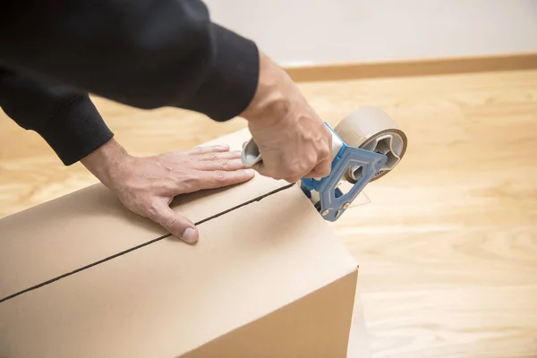 Manos de un hombre usando un dispensador de cinta para sellar una caja de envío — Foto de Stock