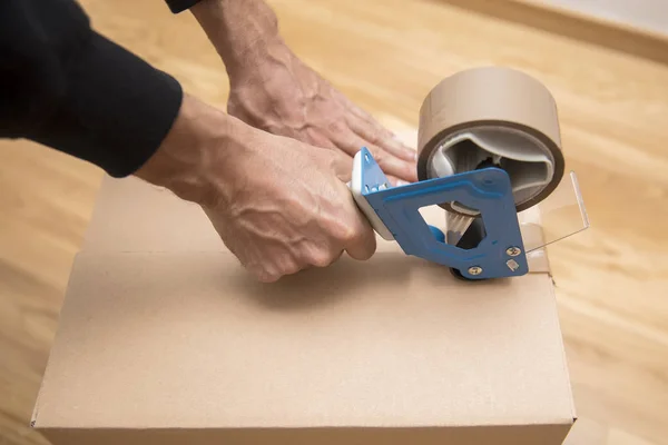 Manos de un hombre usando un dispensador de cinta para sellar una caja de envío — Foto de Stock