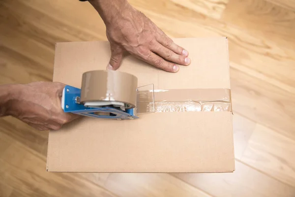 Manos de un hombre usando un dispensador de cinta para sellar una caja de envío — Foto de Stock