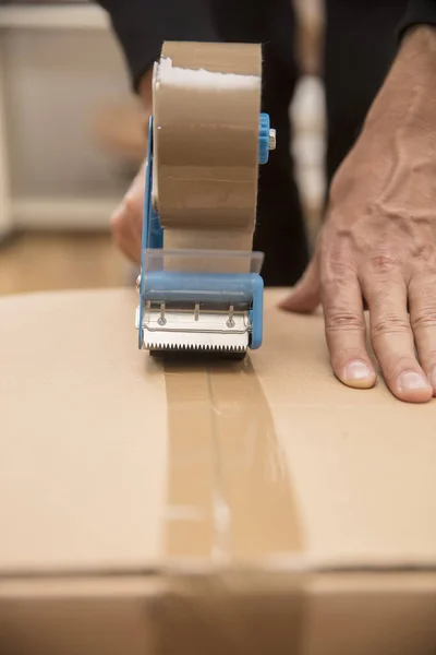 Τα χέρια ενός ανθρώπου χρησιμοποιώντας ένα ακροφύσιο ταινία για να σφραγίσει ένα κιβώτιο αποστολής — Φωτογραφία Αρχείου