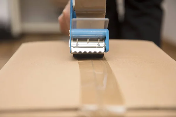 Hands of a man using a tape dispenser to seal a shipping box — Stock Photo, Image