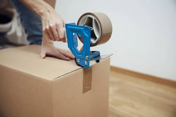 Hands of a man using a tape dispenser to seal a shipping box — Stock Photo, Image