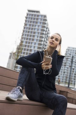 Akıllı telefon ve kulaklıkları ile gülümseyen genç kadın dinliyor 