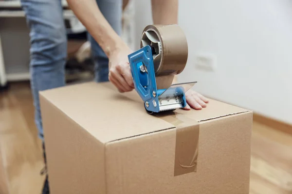 Händerna på en man med hjälp av en tejp Dispenser för att täta en leverans låda — Stockfoto