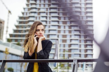 Arka planda ofis binaları ile sokakta bir cep telefonu ile çalışan Yönetici kadın
