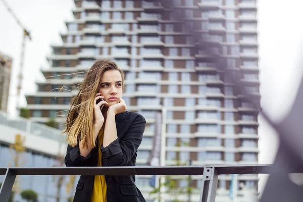 Arka planda ofis binaları ile sokakta bir cep telefonu ile çalışan Yönetici kadın
