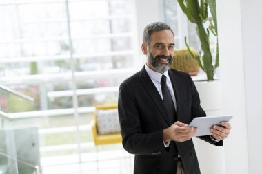 Ofiste çalışan, okuyan ya da bir şey arayan dijital tablet ile Yakışıklı gülümseyen olgun işadamı