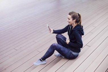 Genç, sportif bir kadın cep telefonu kullanıyor ve merdivenlerde oturuyor.