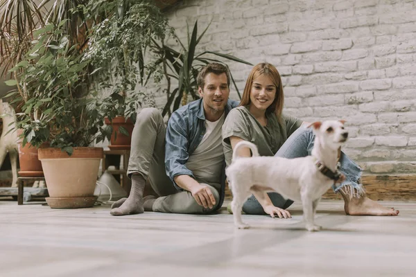 Güzel genç çift rustik oturma odası katta oturan ve sevimli beyaz köpek ile oynarken